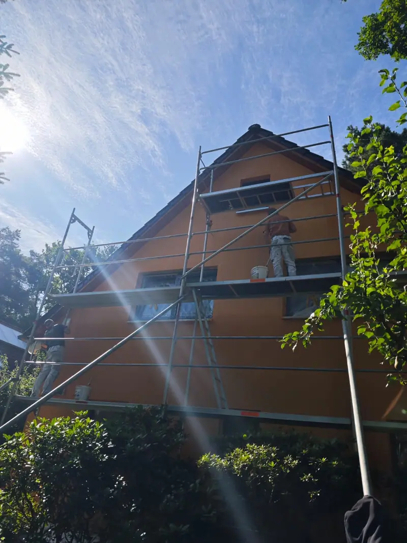 Malerarbeiten an einer orangefarbenen Hausfassade mit Gerüst