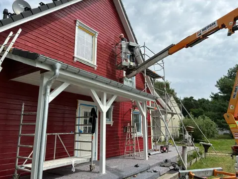 Rote Holzfassade mit Arbeitsbühne und vorbereiteten Fensterbereichen