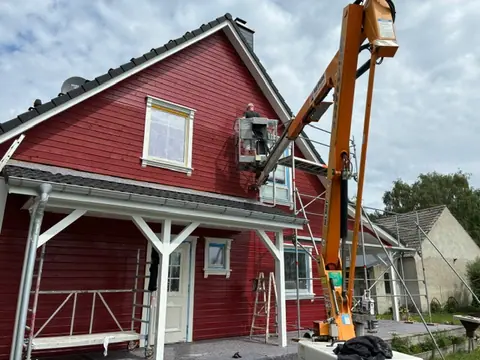 Arbeitsbühne an einem roten Holzhaus während Fassadenarbeiten